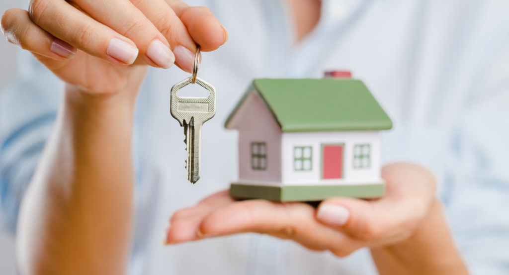 Women holding house key with miniature green and red house in palm